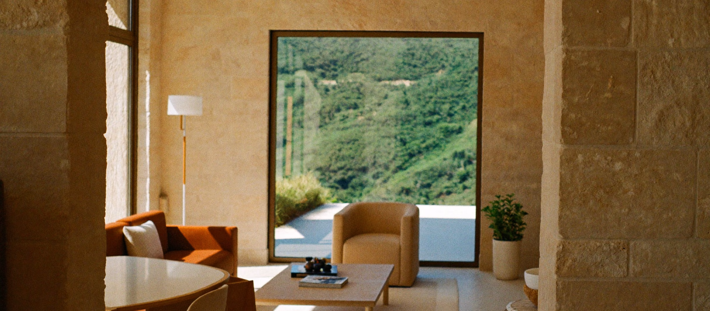 Bright modern interior with warm stone walls and windows onto green hills.