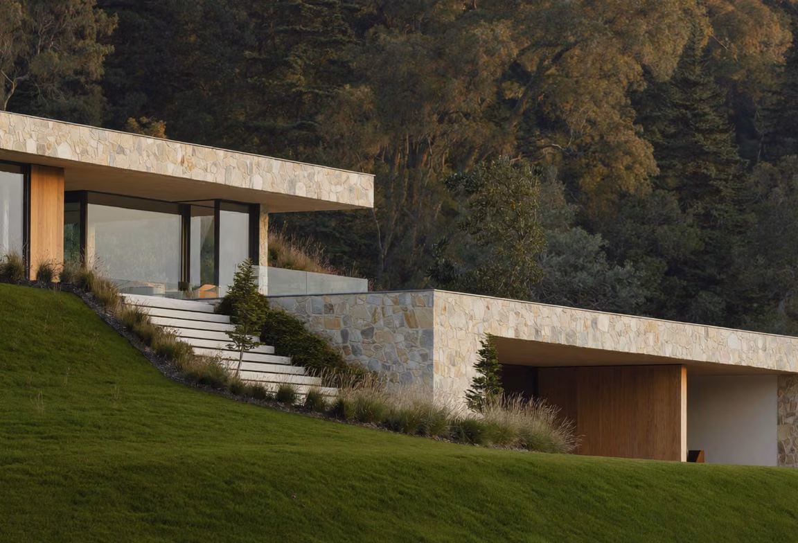 Warm limestone residential building set against a green hillside.
