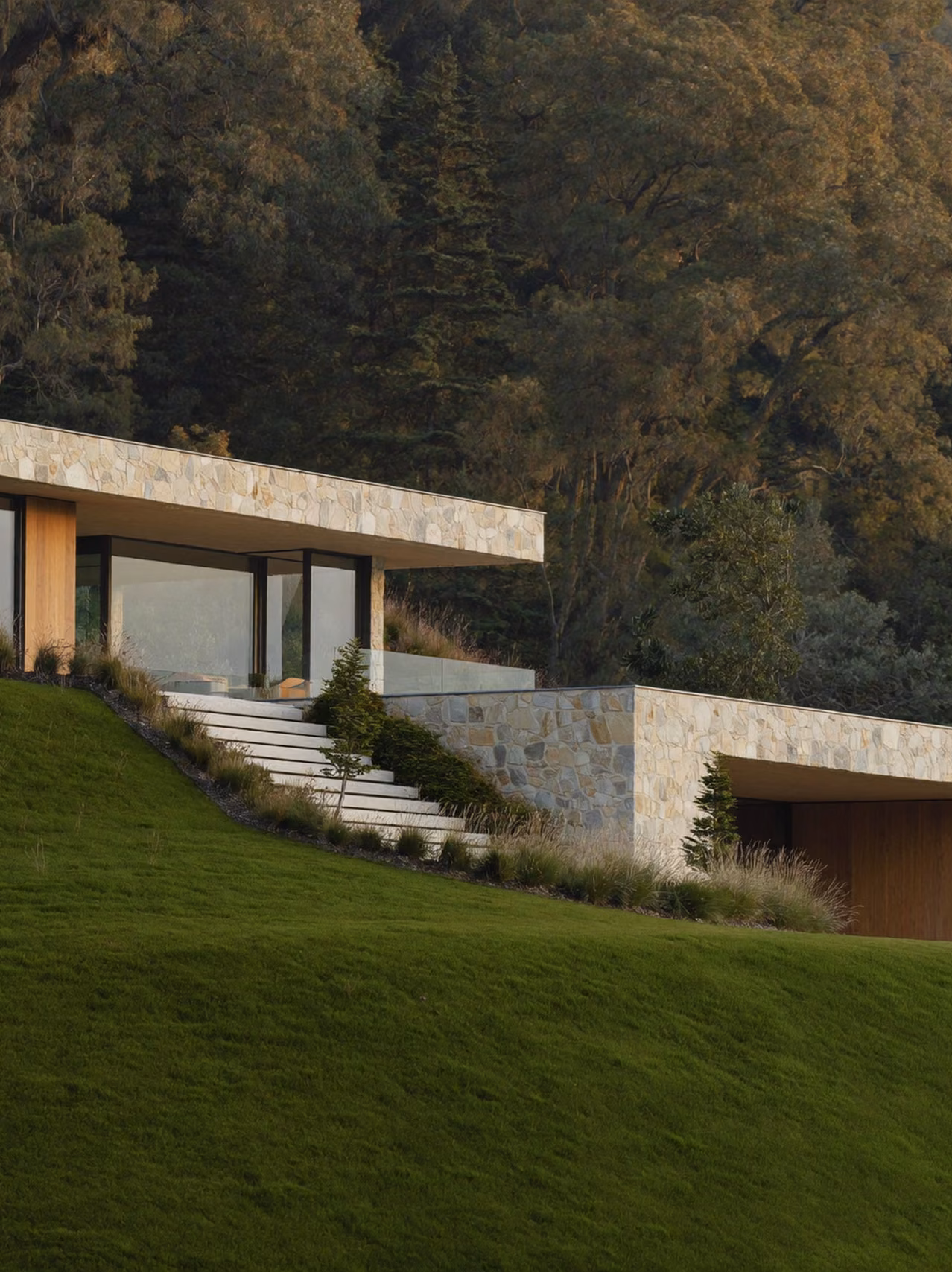 Modern limestone building on a green hillside in soft morning light.